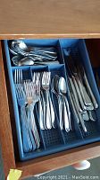 Full drawer view containing assortment of stainless steel cutlery separated in sections for spoons, forks, and knives.