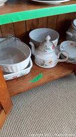 Photo showing teapot with lid, creamer, sugar bowl, salt and pepper shakers, gravy boat, and serving dishes on wooden shelf.