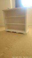 Front view of white painted wood bookshelf with three shelves and scalloped bottom edge showing slight wear.