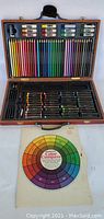 Full view of open wooden art case with colored pencils, oil pastels, and color wheel chart below case.