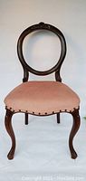 Front view of balloon back chair showing carved wooden frame and pink upholstered seat.