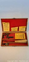 Full view of wooden box with red felt lining holding the checkering tool set including the wooden handle, multiple metal cutters, and instruction cards.