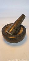 Granite mortar with pestle resting inside, angled side view showing interior of mortar and shape of pestle