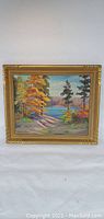 Full view of framed oil painting showing a lakeside autumn landscape with vivid orange foliage and a calm lake.