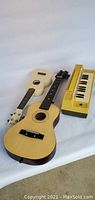 Three musical instruments shown: a white ukulele, youth acoustic guitar, and yellow Mini Organ keyboard
