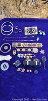 Full view of assortment of costume jewelry laid on purple cloth including bangles, rings, earrings, bracelets, brooches, and pins.
