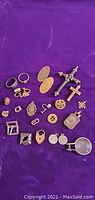 Overview of all costume jewelry pieces arranged on purple background, showing varied types and styles including rings, earrings, lockets, buttons, crosses, and buckles