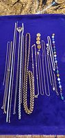 All costume jewelry chains laid out on a dark blue cloth, showing variety of styles, sizes, and finishes including silver-tone and gold-tone chains, some delicate and some chunky.