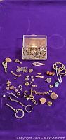 Assorted costume jewelry findings including earring backs, small charms, pendants, and clasps arranged on purple cloth with a small clear plastic box