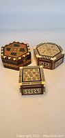 Front view of three finely inlaid wooden boxes, two hexagonal and one square, showing detailed geometric patterns on the lids and sides.