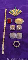 Photo of all nine sterling silver jewelry pieces laid out on a purple background including bracelet/pendant, brooches, pin, ring and earrings