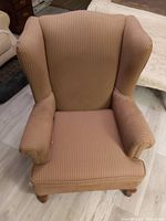 Front view of brown wingback upholstered chair showing seat and curved armrests with wooden legs