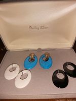 Photo of earrings set in original box with white, blue and black oval hoop attachments displayed around sterling silver pierced earring bases.
