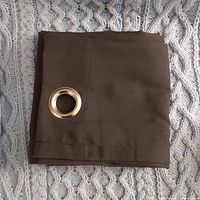 Folded navy blue curtain panel with a gold metal grommet ring placed on a textured light blue knit background. Photo highlights fabric and grommet detail.