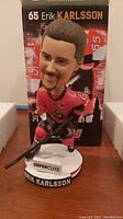 Front view of Erik Karlsson bobblehead showing detailed face, Ottawa Senators jersey with '65' and captain's C, white base with 'SUPER CUTS' and 'ERIK KARLSSON' text, and original box behind.