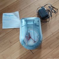 Top-down view of Febreze Scentstories device alongside power adapter and instruction manual on wooden floor
