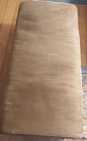 Top view of rectangular foot stool bench, showing smooth light brown upholstery with stitched lines across the middle.