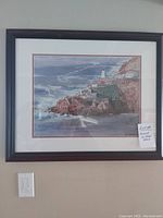 Frontal view of the framed painting showing the ocean, cliffs, and lighthouse scene with note attached.