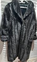 Front view of long black faux fur coat on hanger showing texture, collar, sleeves, and length.