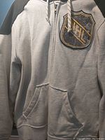 Front view of gray NHL blazer jacket with NHL logo patch, zipper, pouch pocket, and drawstring hood
