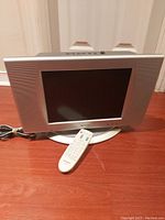 Front view of Sharp TV with remote placed in front, showing silver frame and oval base stand on wooden floor.
