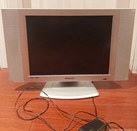 Front and side view of a small Polaroid TV showing screen and speakers, with power adapter cable on floor.