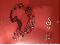 Full view of the musical wall decor showing the trumpet player figure integrated with metal music notes on a red wall, with smaller separate metal musical notes hanging below.