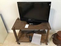 Full view of the Dynex 26 inch TV placed on the wooden TV stand with remote and manual.