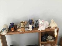 Shelf with assorted decorative ceramic figurines including cats, duck, globe, bell, metal mug, and wooden barrel
