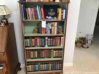 Front view of the wooden bookcase filled with books and assorted items on top.