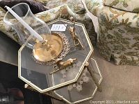 View of brass octagon end table with glass shelves showing brass candle holder with glass hurricane shade on top, two brass animal figurines on table surface