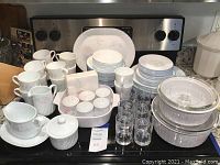 Full view of Corelle Impressions pattern dishes including plates, cups, glassware, and casseroles on kitchen counter.