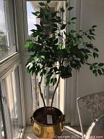 Faux tree with realistic green leaves and three main trunks in a heavy brass pot with handles.