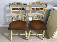 Front view of two Hitchcock chairs showing cream-colored frames with dark floral stenciling and dark wood seats.