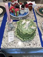 Photo showing the Holland Mold ceramic cabbage dish with three white rabbits on the lid and the decorative candle holder with a pink candle on a countertop.