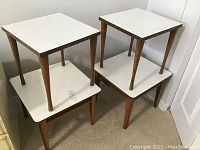 Four Mid-Century Modern style side tables, two stacked on top of two others, all with wood legs and white Formica tops.