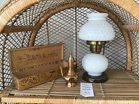 Overall view showing milk glass hobnail lamp, hand painted wooden box, and small brass decorative teapot arranged on a wicker shelf