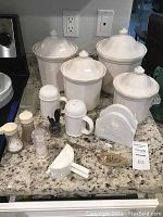 Full view of the set of 4 white ceramic Pfaltzcraft canisters with lids on counter, along with various white kitchen decor items including salt and pepper shakers, napkin holder, and small kitchen tools.