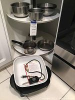 Photo of multiple stainless steel mixing bowls, a small saucepan, frying pan placed on shelving units