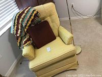 Yellow swivel rocker chair with tufted backrest, brown throw pillow, and multicolored Afghan. Shown near window and wooden furniture.