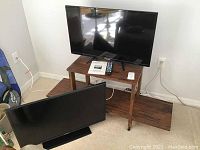 Overall view of two flat screen TVs and wooden TV stand