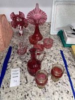 View of entire cranberry glassware collection including vases, jars, pitcher, swan figurine, and drinking glasses.