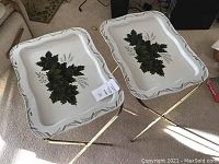 Pair of vintage folding tray tables with white trays featuring green leaves pattern and gold-toned folding metal legs.