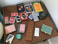 Full view of the lot on a wooden table showing assorted decks of playing cards, game books, cribbage board, and electronic organizer.