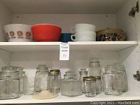 Overview photo showing vintage Pyrex mixing bowls on top shelf with assorted glass storage jars and mason jars below.