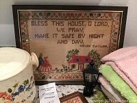 Photo of large framed cross stitch with prayer text, night light, and floral container.
