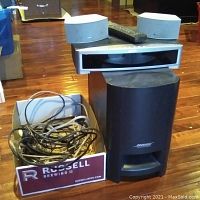 Photo of Bose PS3-2-1 II powered speaker unit, control box, two small Bose speakers, remote on top, and a box with cables.