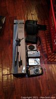 Lot of four cameras, Nexxtech tripod in box, three camera cases on hardwood floor