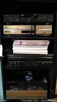 Stacked electronics showing Toshiba DVD player on top, Sony VHS player middle, Pioneer laser karaoke player below and wooden turntable base at bottom.