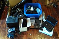 Photo showing a box and assorted electronics including handheld phones, electronic dictionary, headsets, and small devices on wooden floor